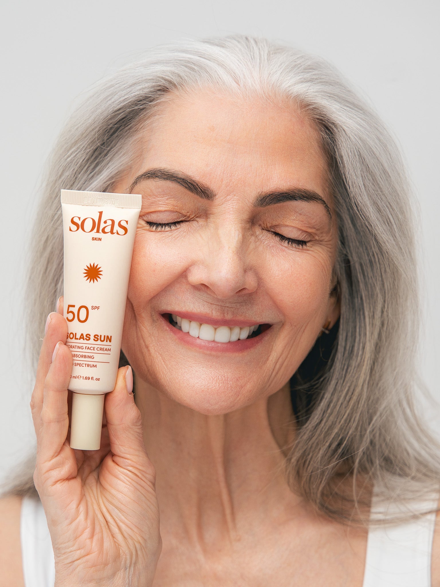 Woman holding a Solas Sun tube against a plain background