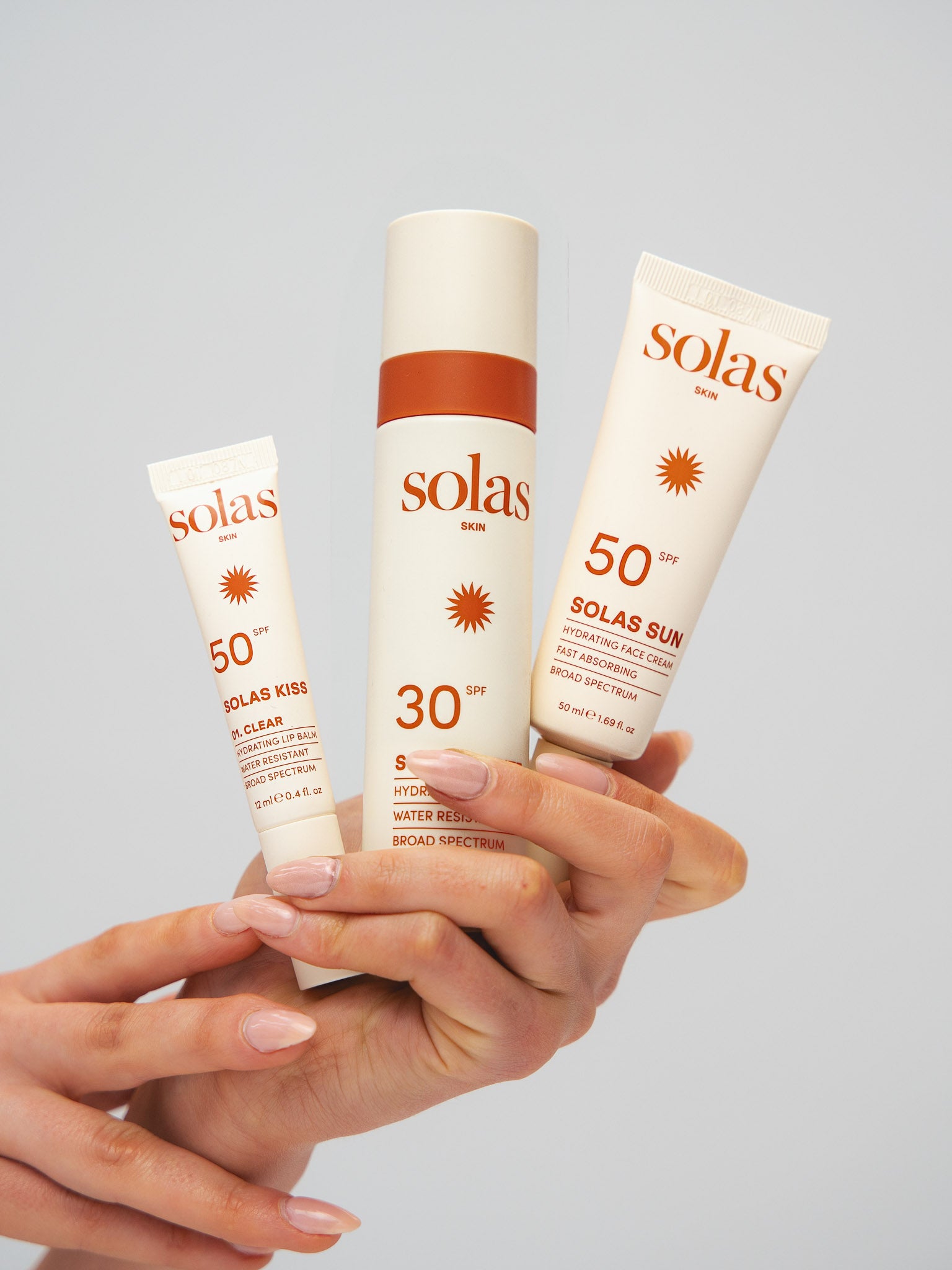 Hand holding three Solas sunscreen products against a gray background