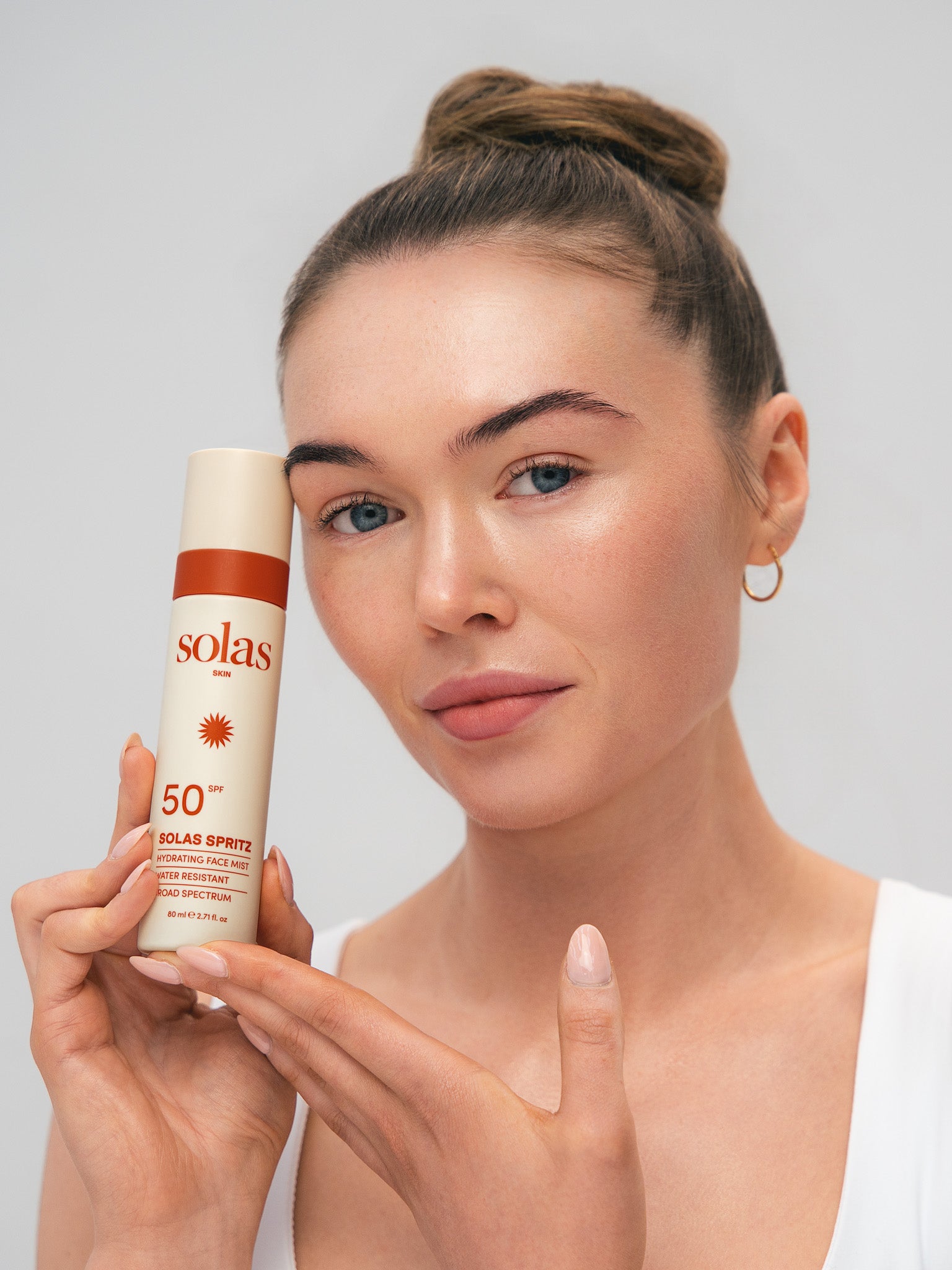 Woman holding a Solas Spritz spray bottle against a plain background