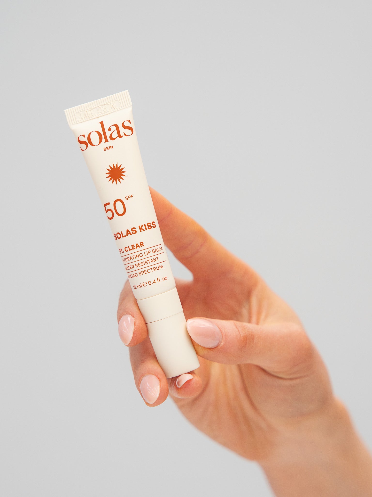 Hand holding a Solas Kiss lip balm with SPF 50 on a gray background