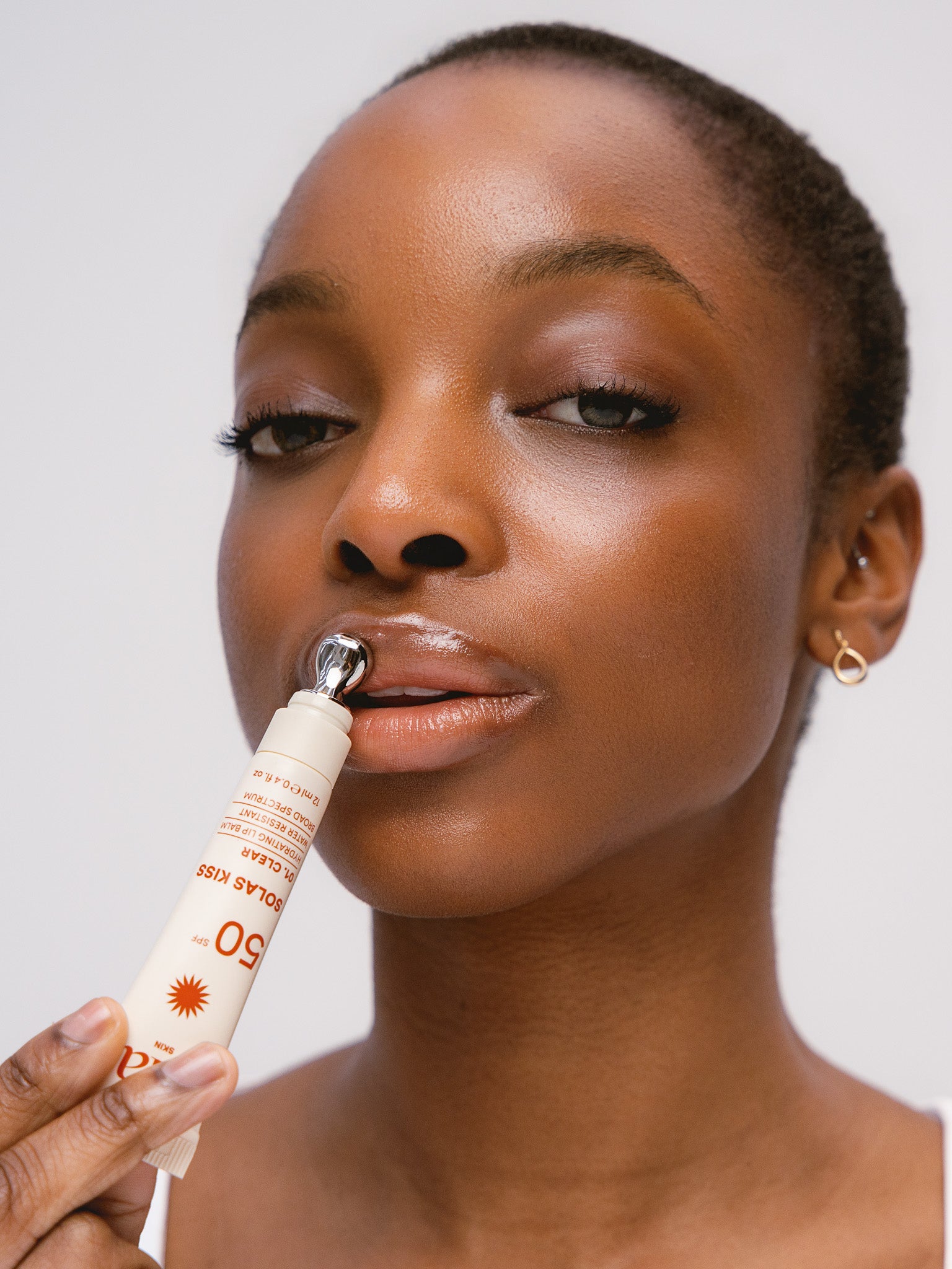 Woman applying Solas Kiss lip balm to her lips, using metal applicator tip
