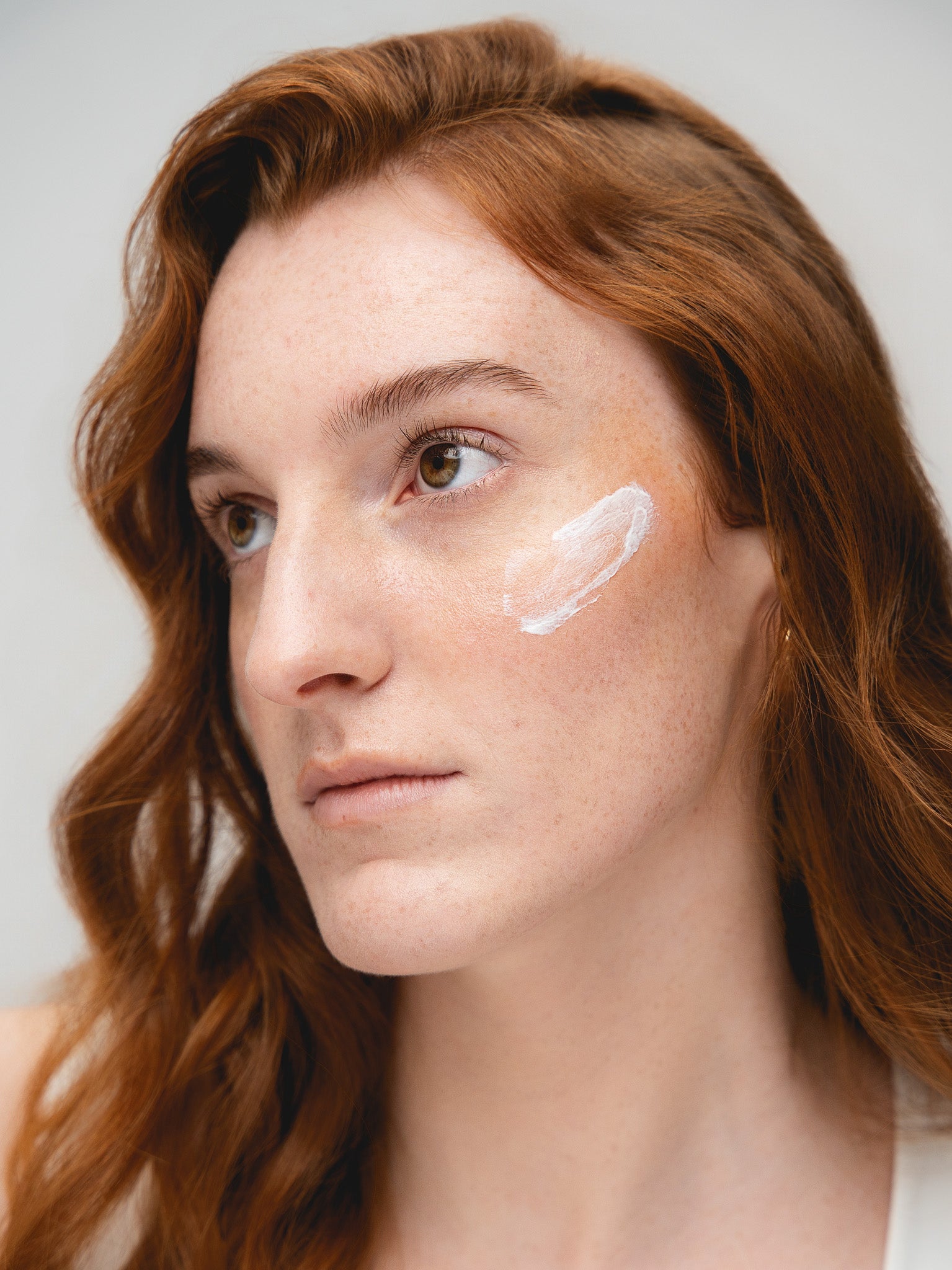 Woman with a small amount of Solas Sun cream on her cheek against a neutral background