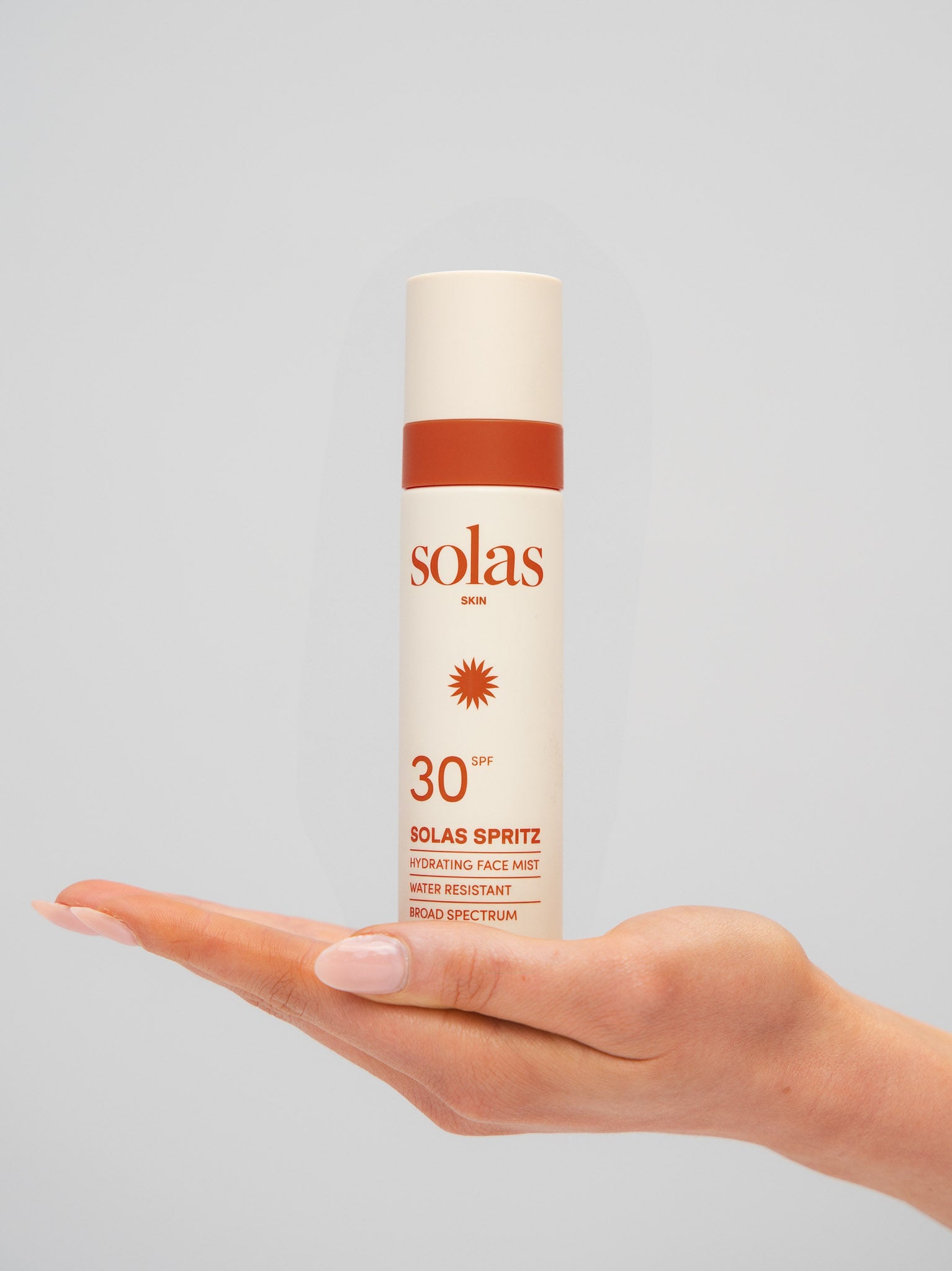 Solas Spritz hydrating face mist held in a hand against a grey background