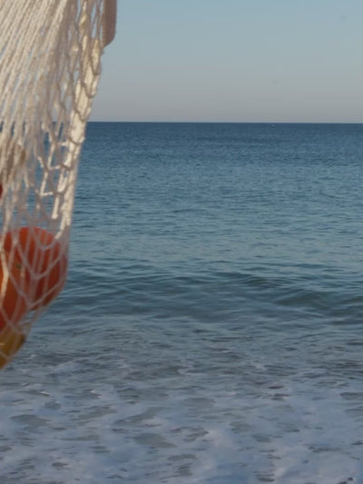 Solas Spritz swaying in a netted bag in front of the sea.